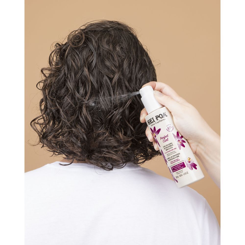 Flacon de spray HEI POA Perfect Curl pulvérisé sur des cheveux bouclés.