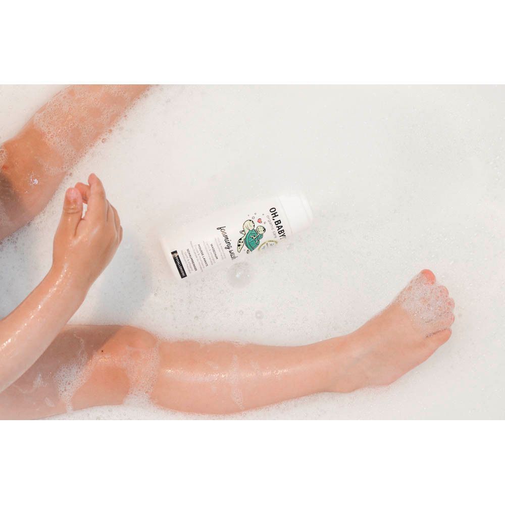 Un enfant dans un bain moussant tient un flacon de mousse lavante Oh Baby!.