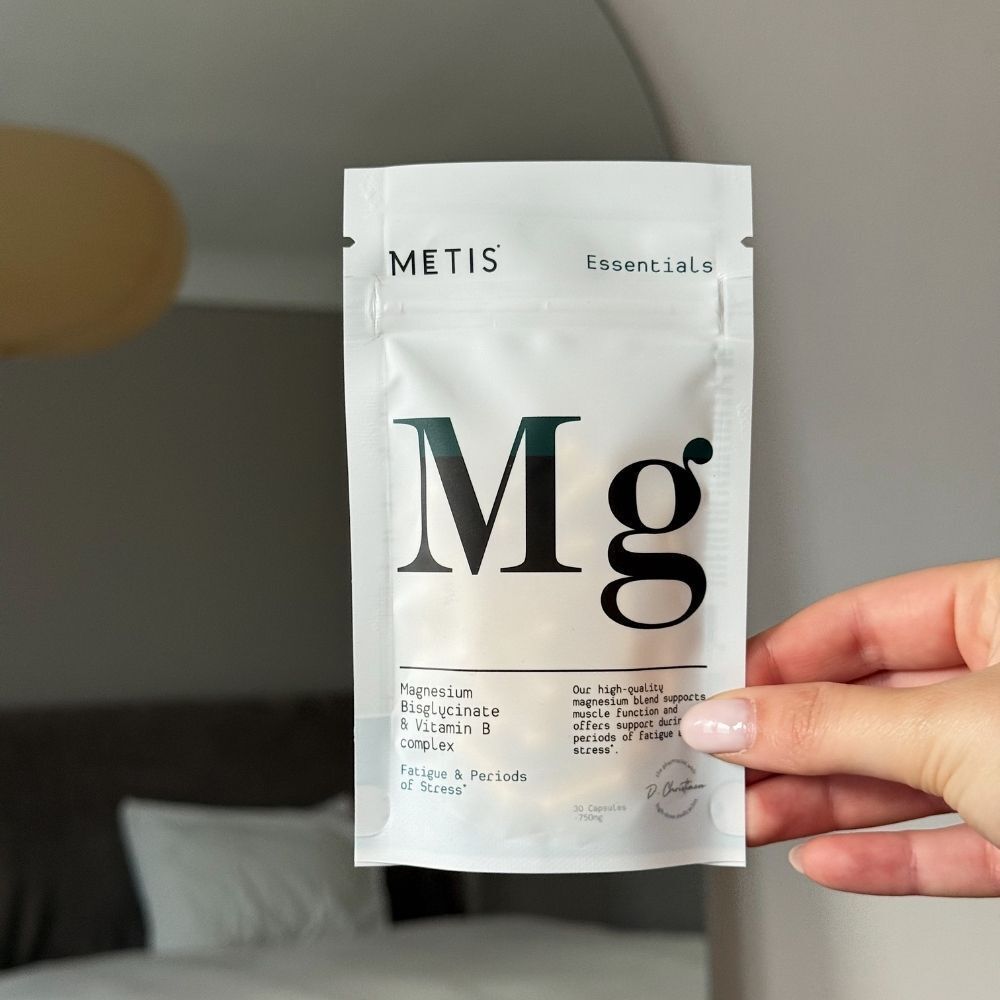 Une main tenant un sachet 'Metis Essentials Mg' contenant du bisglycinate de magnésium.