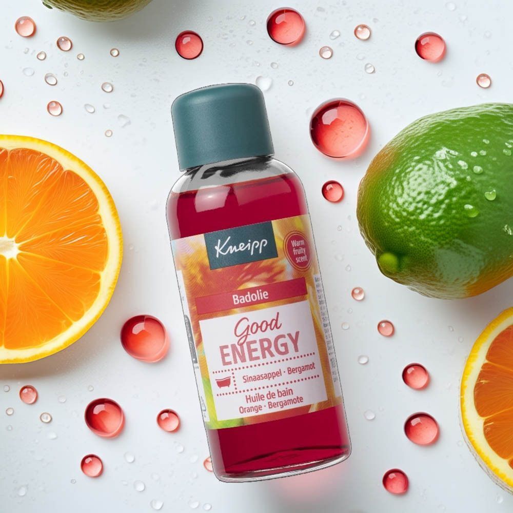 Fles Kneipp Good Energy Badolie omringd door sinaasappels, limoenen en waterdruppels.
