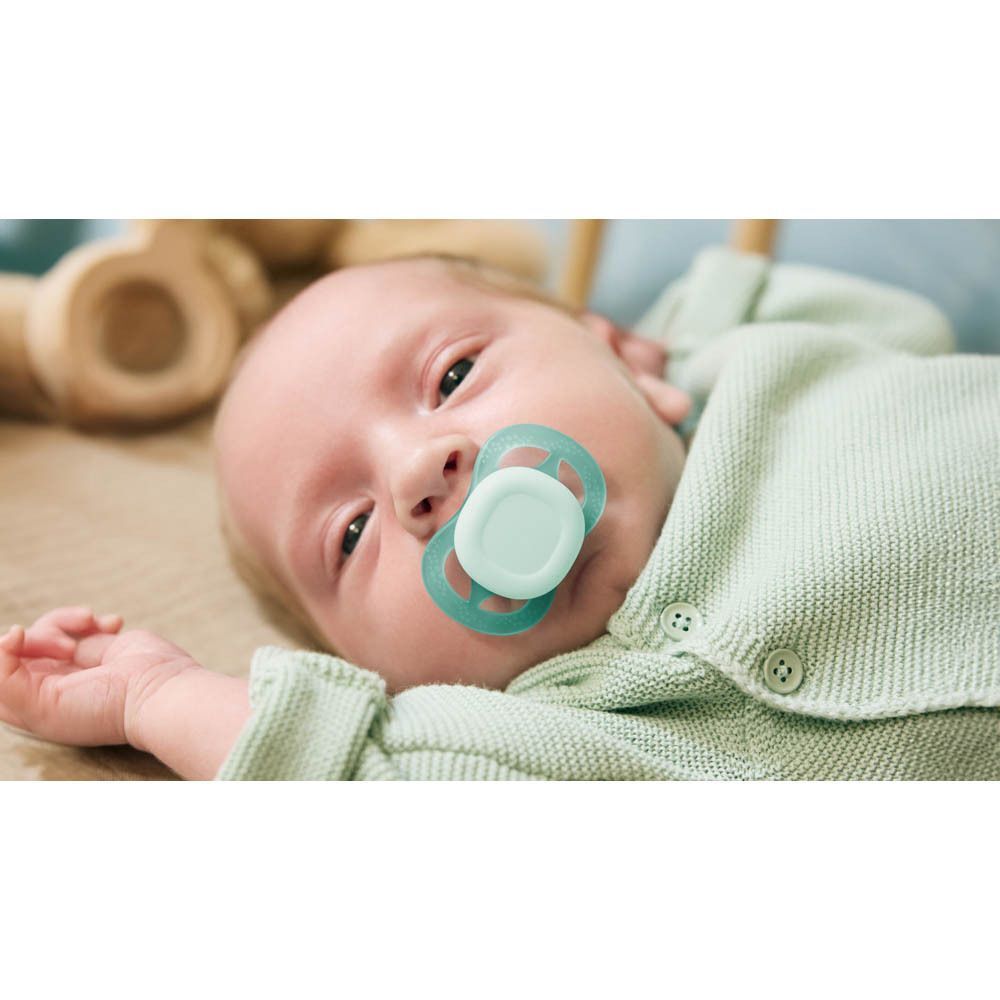 Bébé avec une sucette vert menthe dans la bouche.