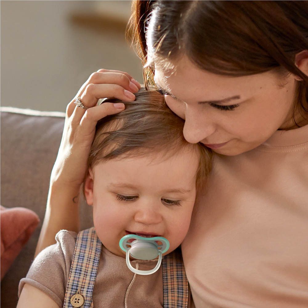 Une femme tient un bébé portant une sucette et lui caresse la tête.