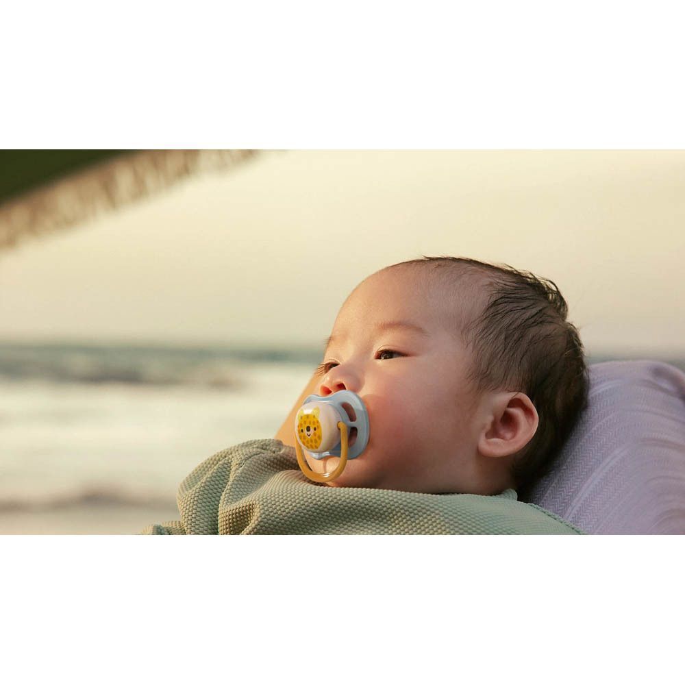 Bébé avec une sucette à motif léopard dans la bouche, sur la plage.