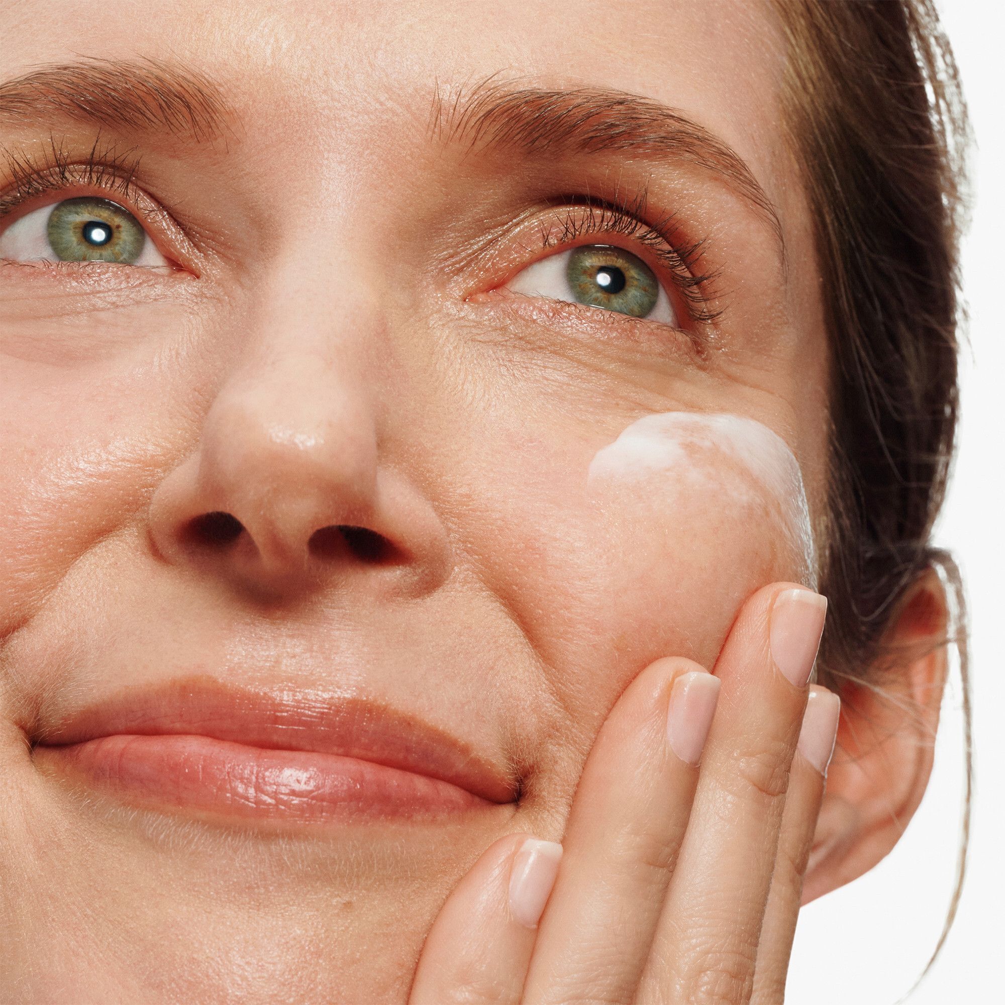 Une femme applique le Clinique Turnaround Overnight Revitalizing Moisturizer sur sa joue.