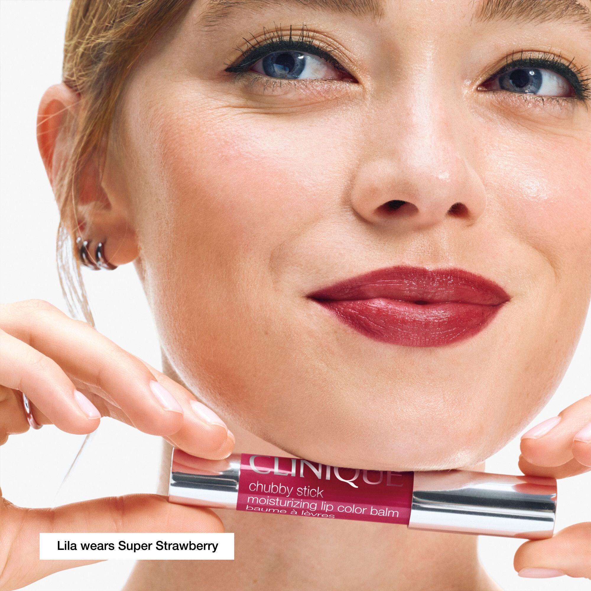 Vrouw houdt CLINIQUE Chubby Stick vast. "Super Strawberry" op de lippen.