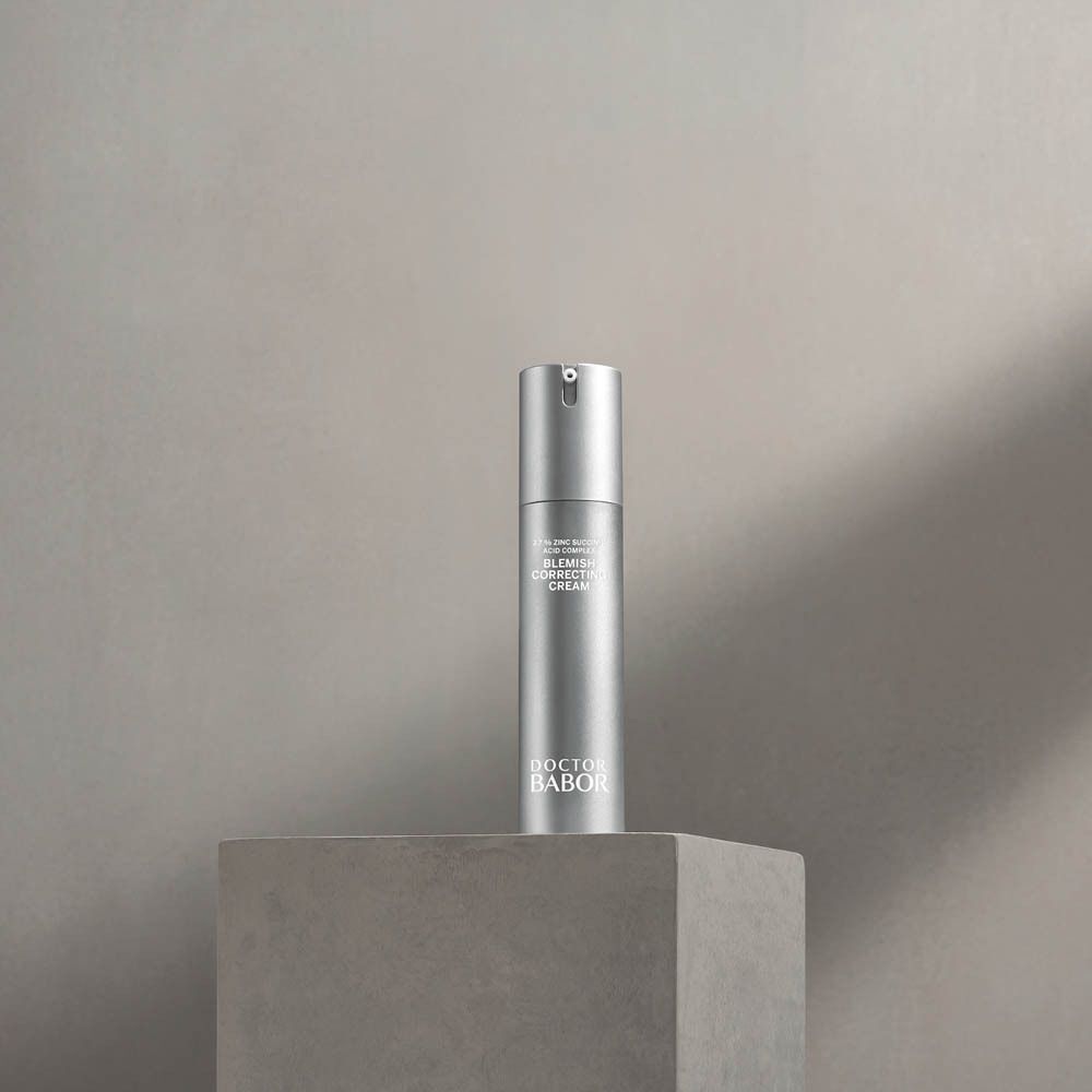 Un flacon argenté de Babor Blemish Correcting Cream sur un socle.
