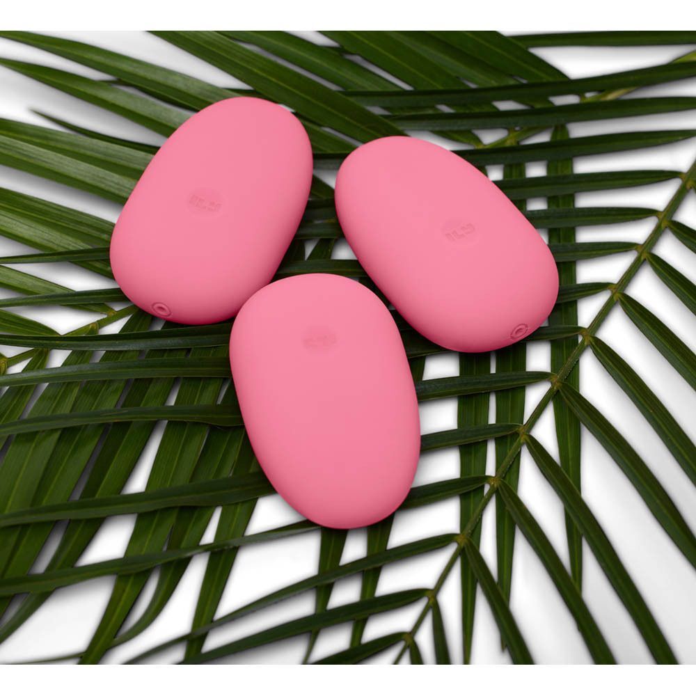 Drie roze, eivormige vibrators op groene palmbladeren.