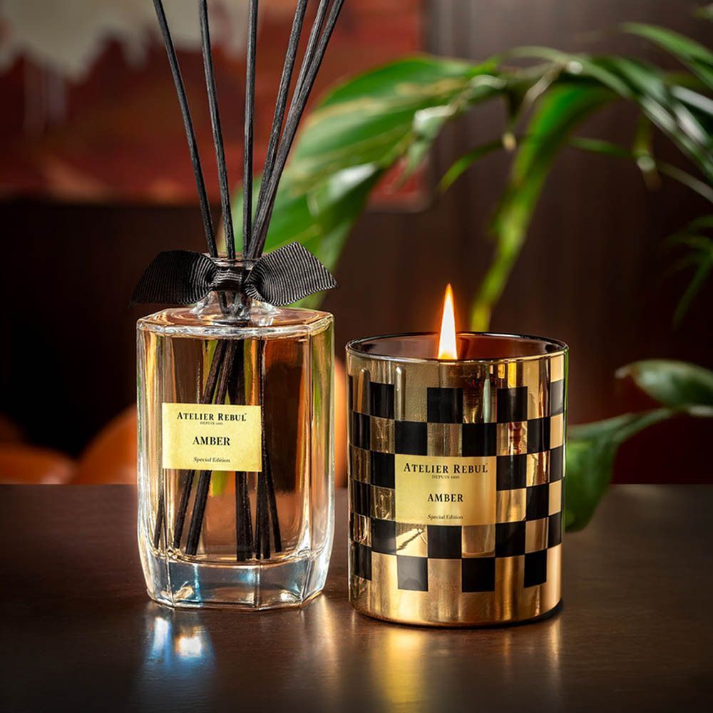 Brandende Atelier Rebul Amber geurkaars en een geurdiffuser in een rek.