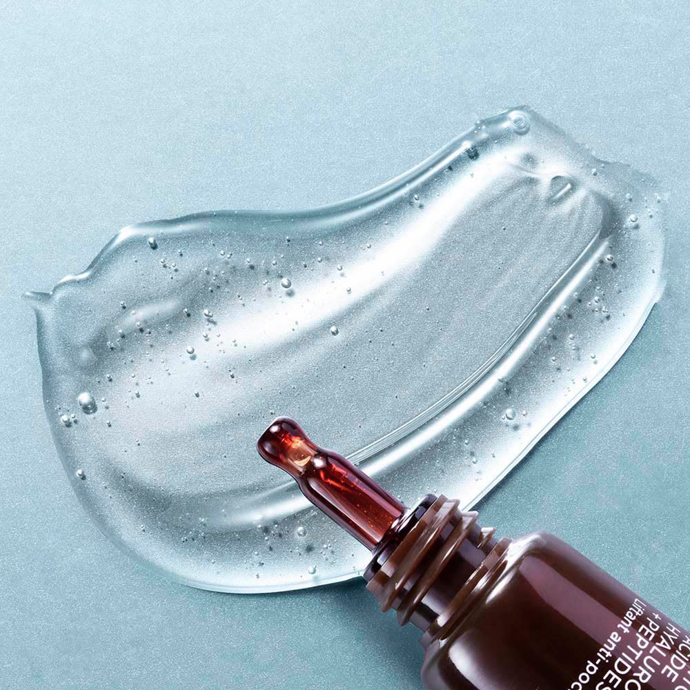 Une goutte de gel transparent pour le contour des yeux avec une pipette sortant d'un tube marron.