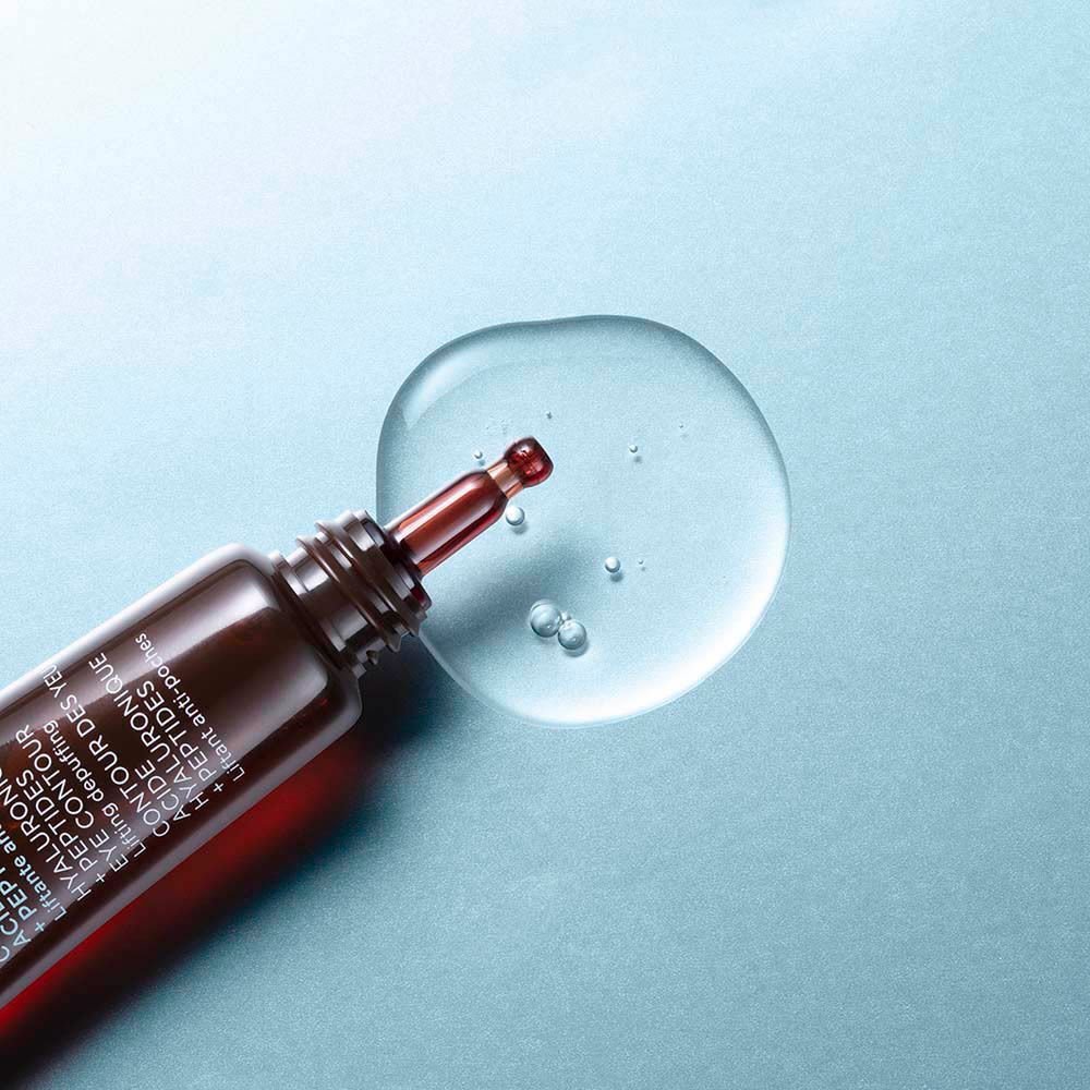 Une pipette de gel transparent pour le contour des yeux sortant d'un tube marron sur fond bleu.