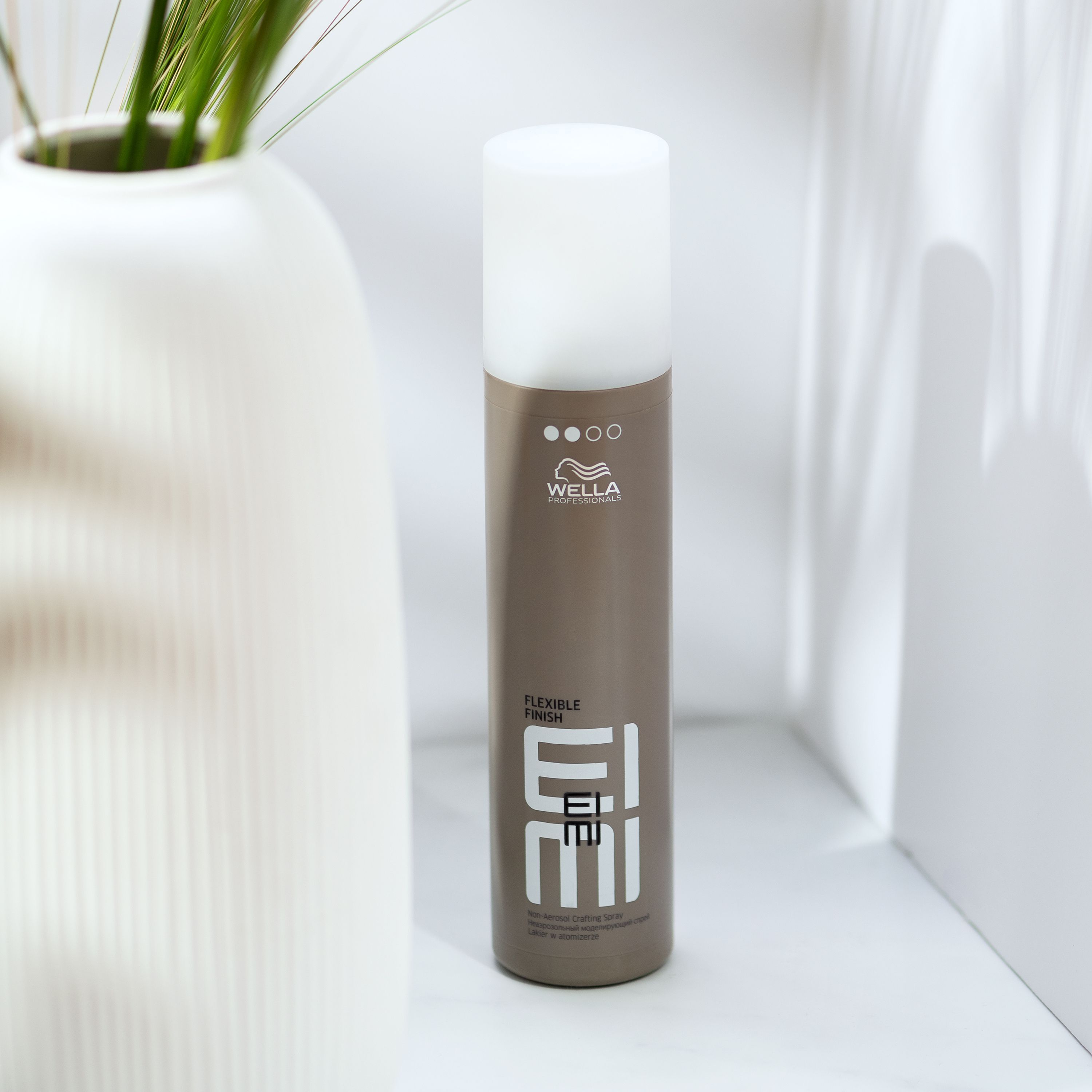 WELLA PROFESSIONALS Flexible Finish haarspray naast een vaas met planten.