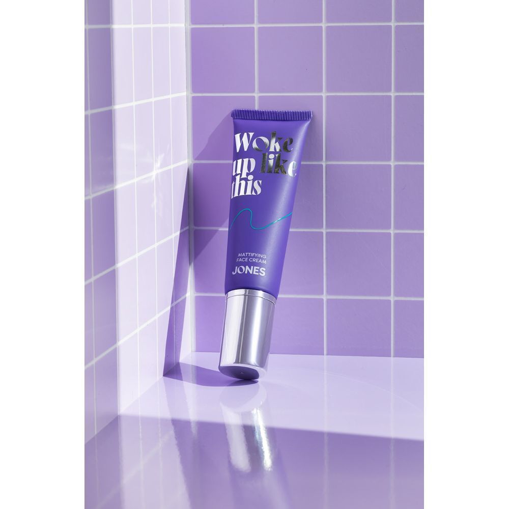 Een tube Jones Mattifying Face Cream in een paarse betegelde hoek.
