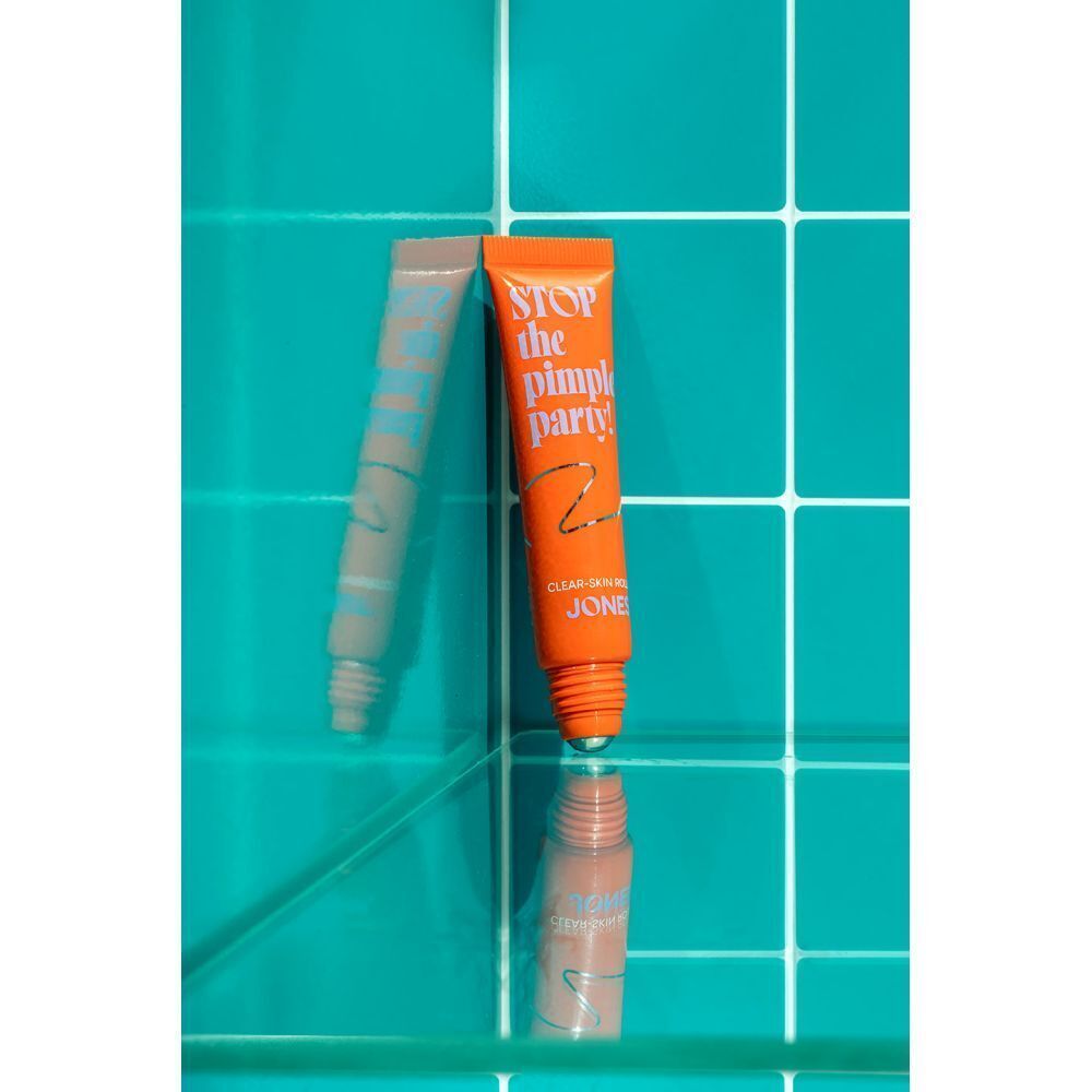 Oranje tube met roll-on applicator, met de tekst "STOP the pimple party! JONES" op een turquoise achtergrond.