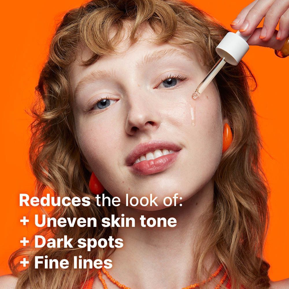 Une femme aux cheveux ondulés reçoit du sérum sur le visage par une pipette.