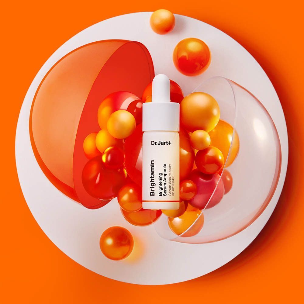 Een flesje Dr. Jart+ Brightamin Brightening Serum Ampoule omringd door oranje bollen.