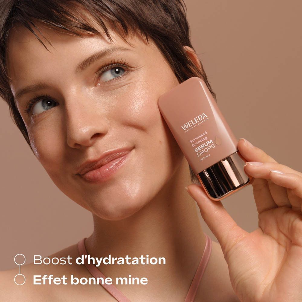 Femme tenant un flacon Weleda Sunkissed Bronzing Serum Drops près de sa joue.