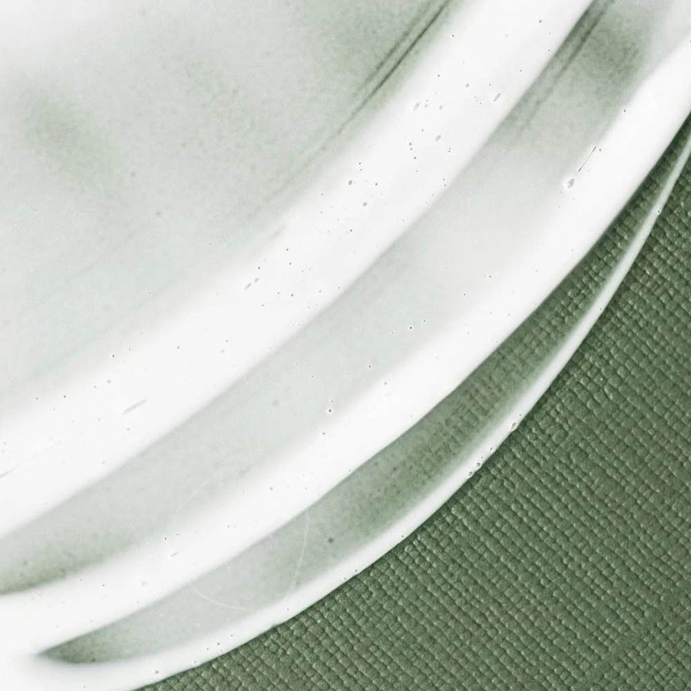 Close-up van een lichtgroene, matte crème textuur met fijne belletjes op een gestructureerde achtergrond.