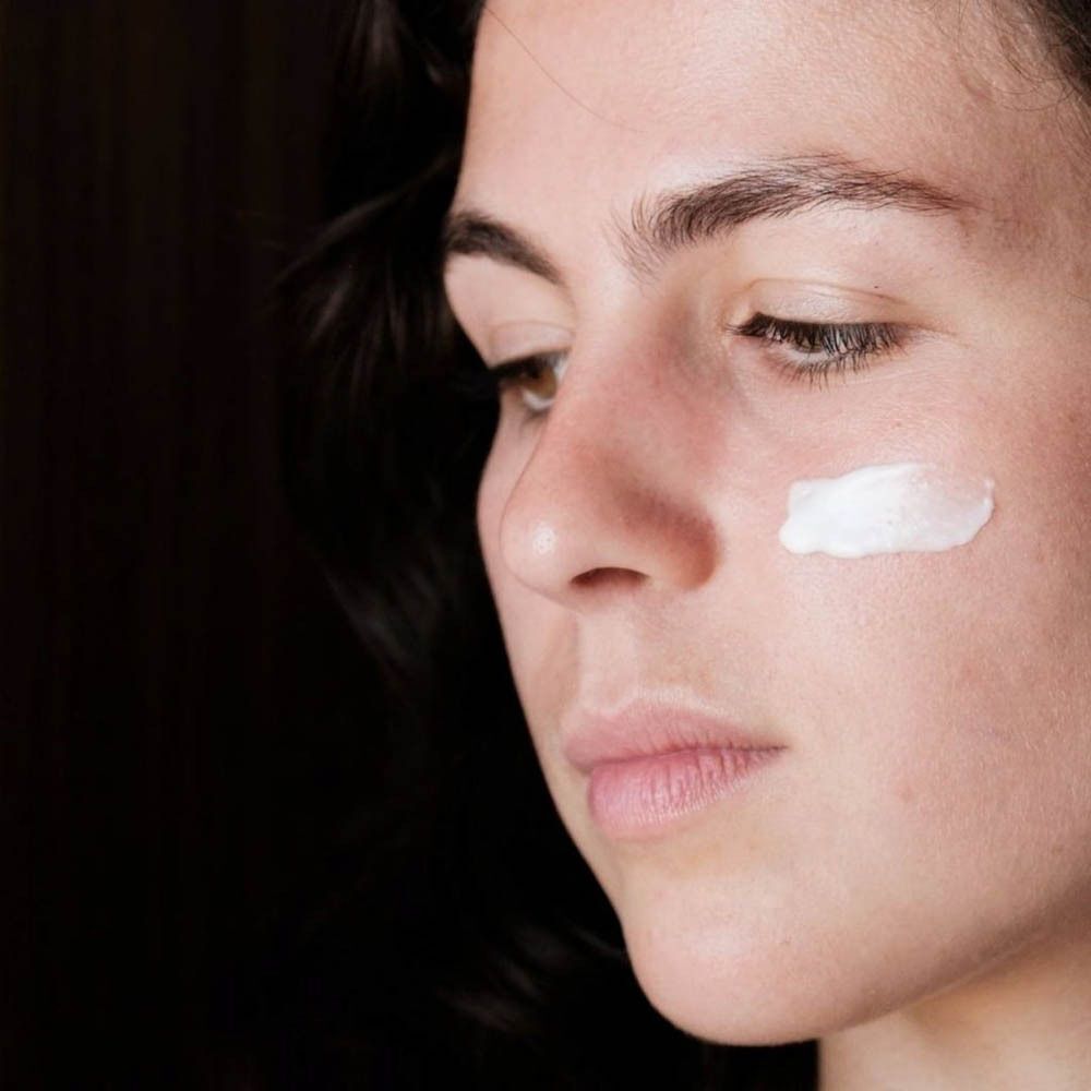 Une femme avec une touche de crème visage matifiante sur la joue.