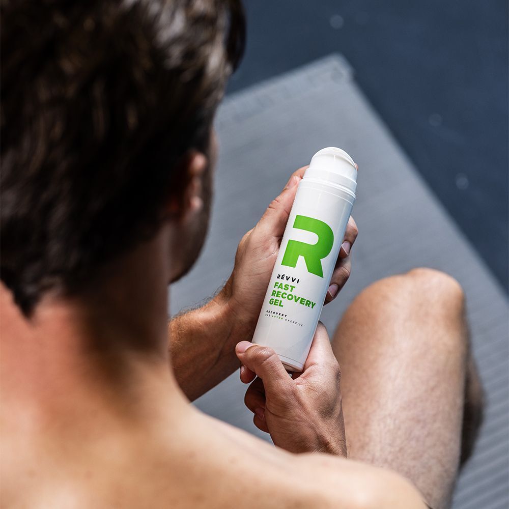 Man houdt een wit pompflesje met groen R-logo en opschrift "RÉVVI FAST RECOVERY GEL" vast.