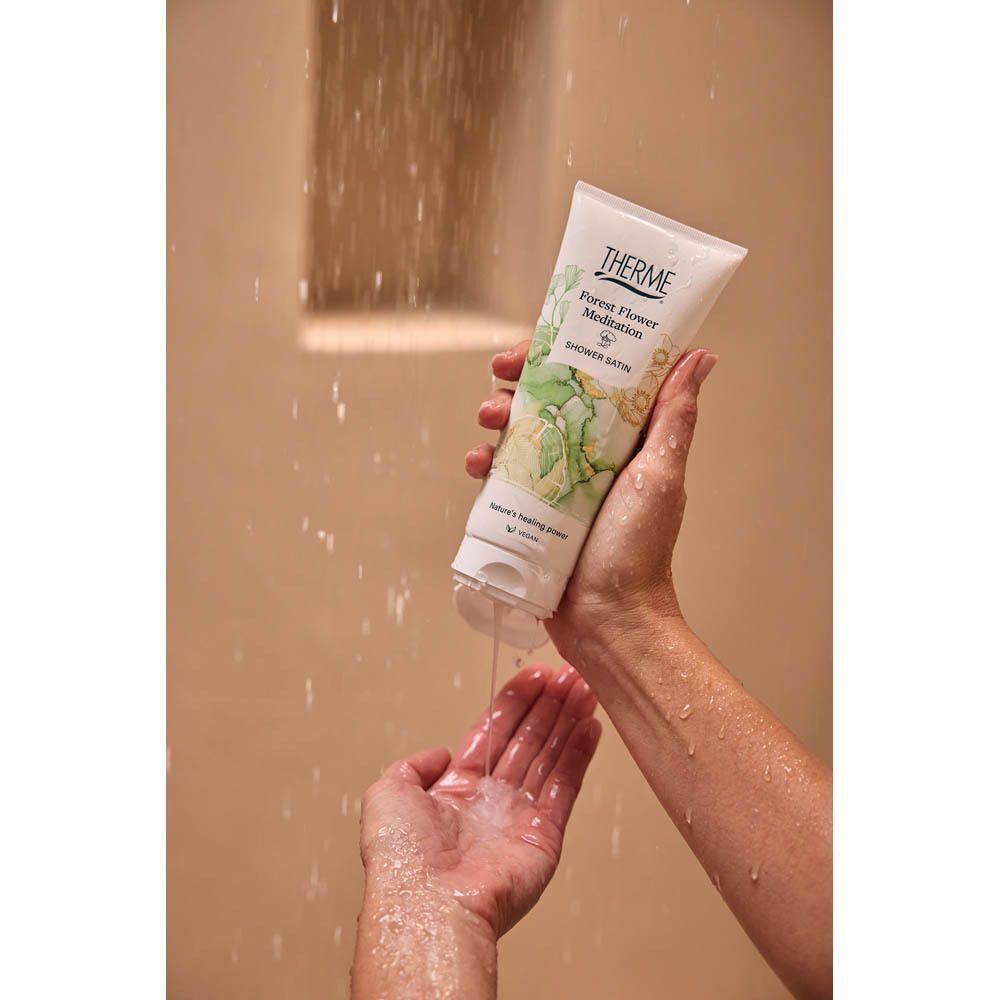 Een hand knijpt Douche Satin 'Forest Flower Meditation' van THERME in de andere hand.