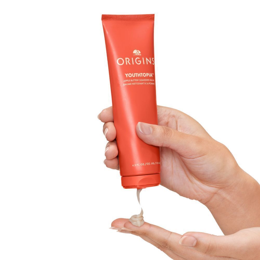 Hand die Origins Youthtopia Apple Butter Cleansing Balm uit een oranje tube knijpt.