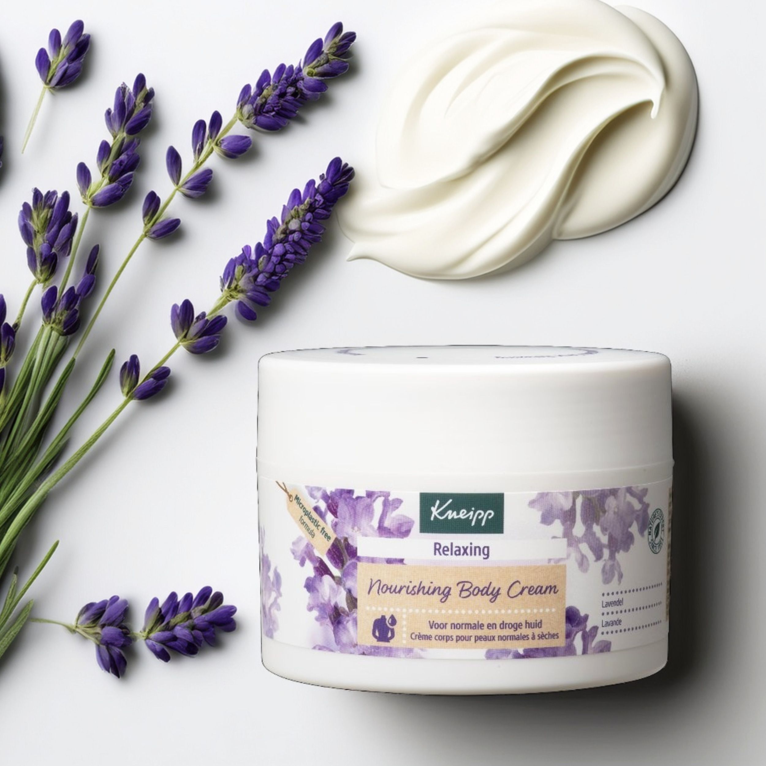 Pot blanc de Crème Corps Nourrissante Relaxante Kneipp à côté de branches de lavande et d'une texture crémeuse.
