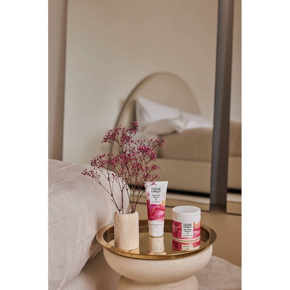 Un tube de Douche Satin et un pot à côté d'un vase fleuri.