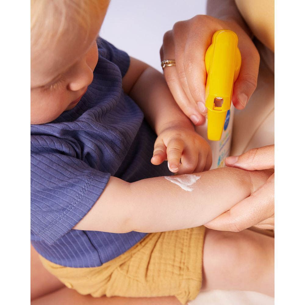 Une main applique de la crème solaire sur le bras d'un bébé.