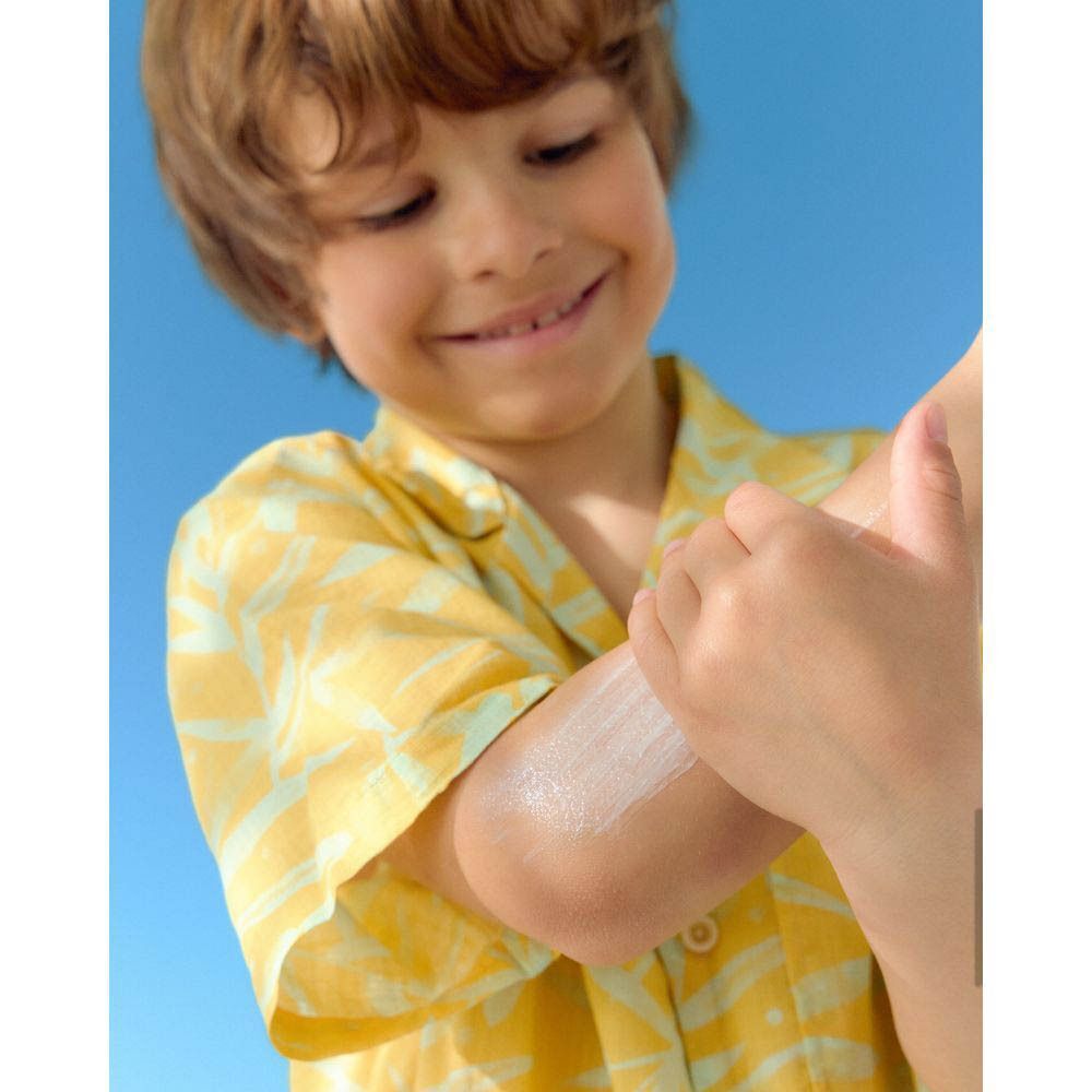 Une main applique de la crème solaire sur le bras d'un garçon souriant.