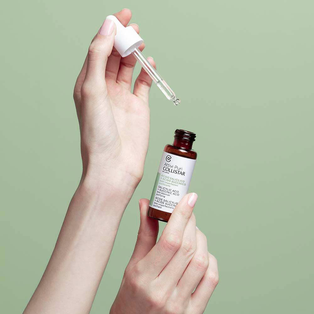 Hand die Collistar Attivi Puri flacon en pipet met serum vasthoudt. Huidverzorgingsproduct.