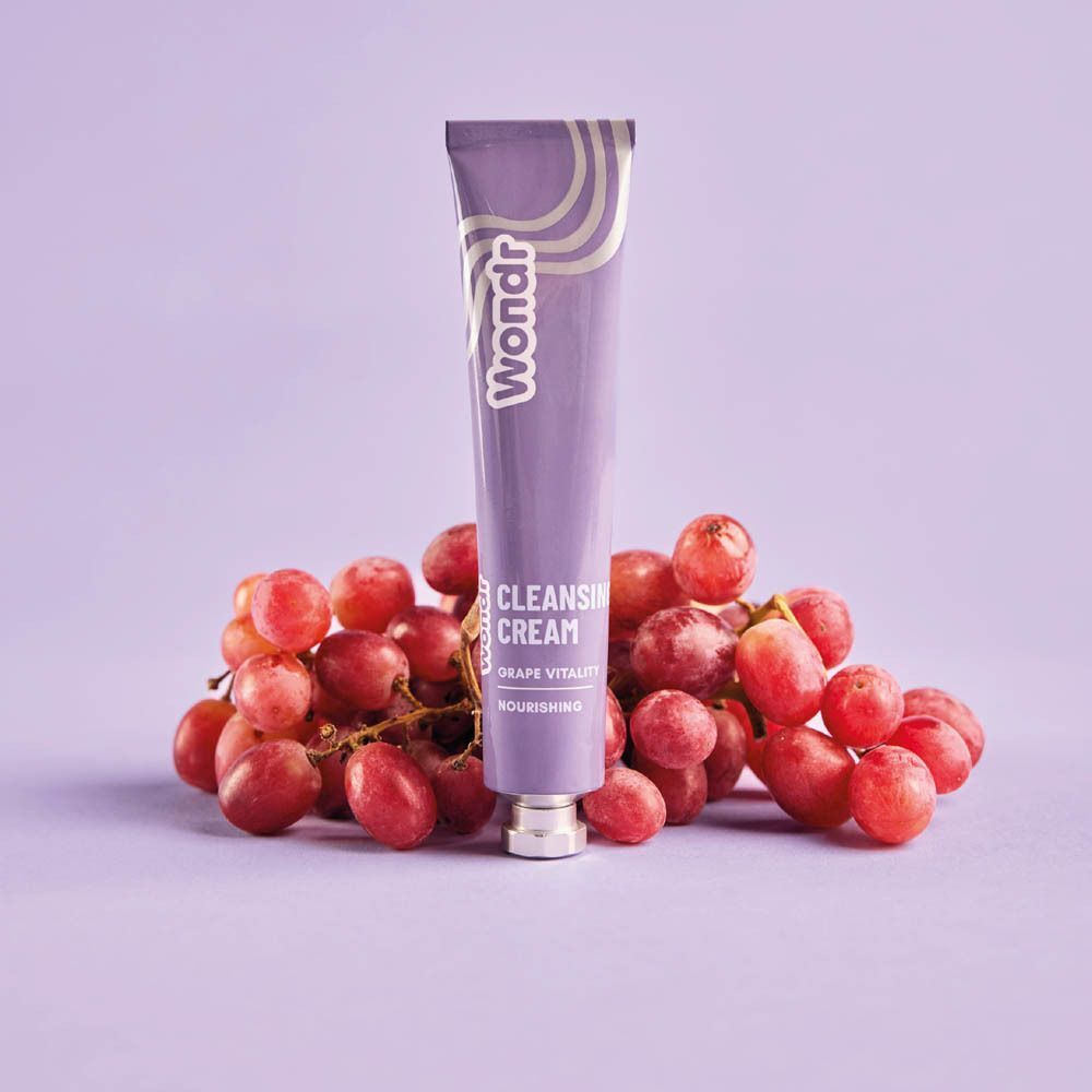 Tube violet WONDR Cleansing Cream Grape Vitality sur des raisins rouges.