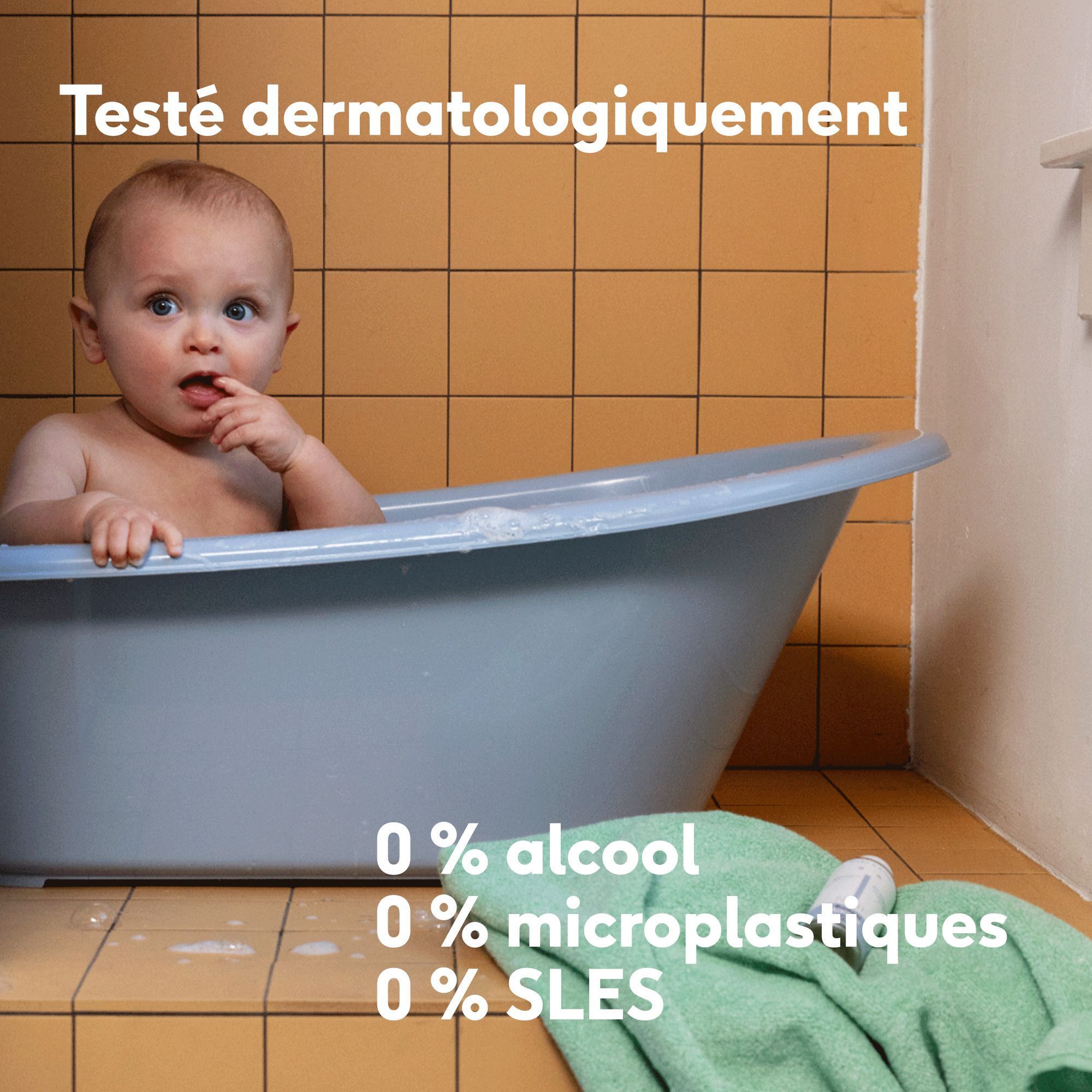 Bébé dans une baignoire, serviette à côté, texte "Testé dermatologiquement".