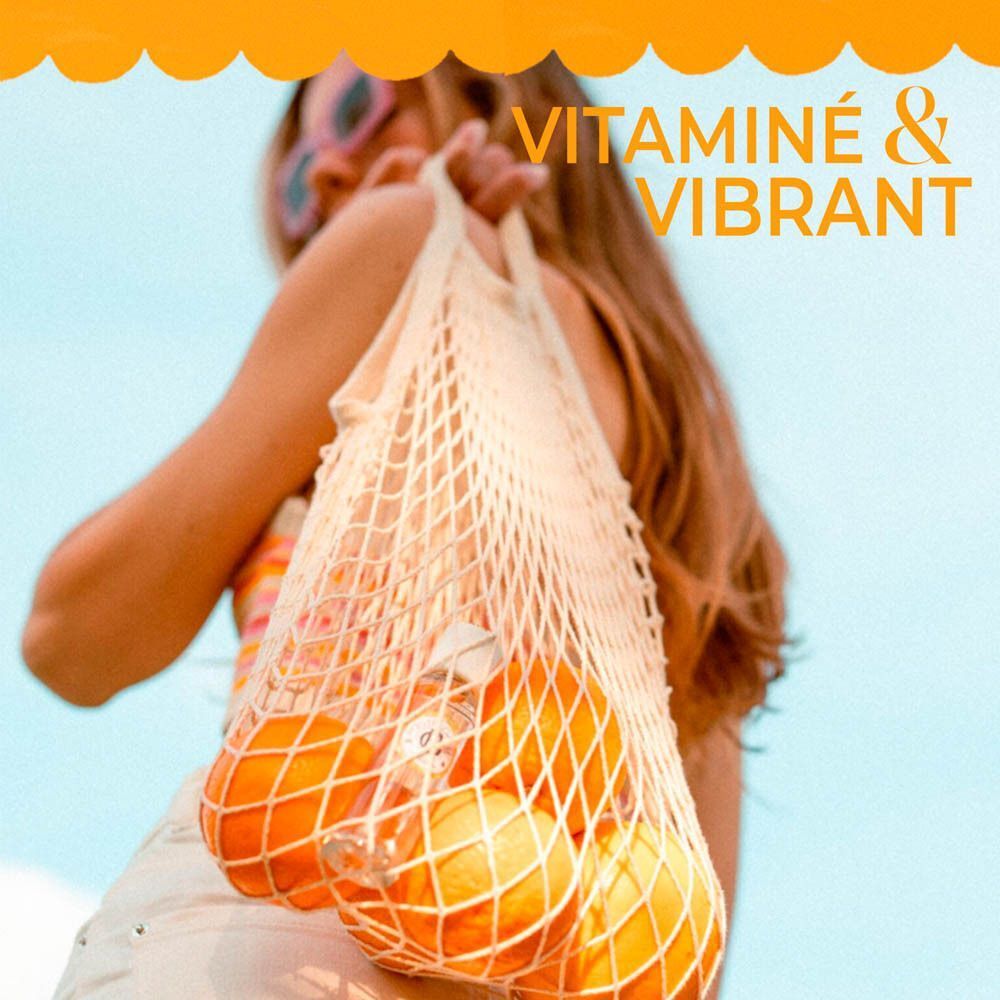 Femme portant un sac en filet rempli d'oranges, texte : Vitaminé & Vibrant.