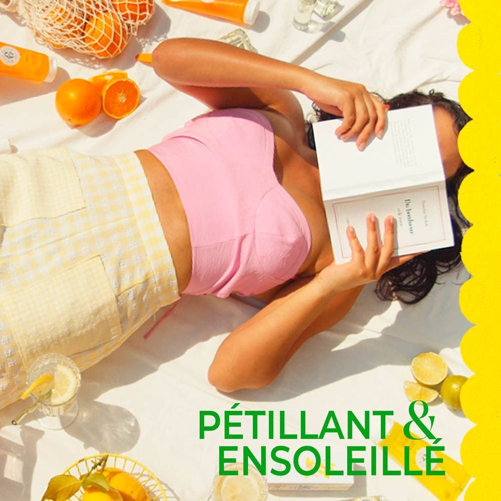 Femme allongée lisant un livre, fruits et gel douche Roger & Gallet sur une couverture.