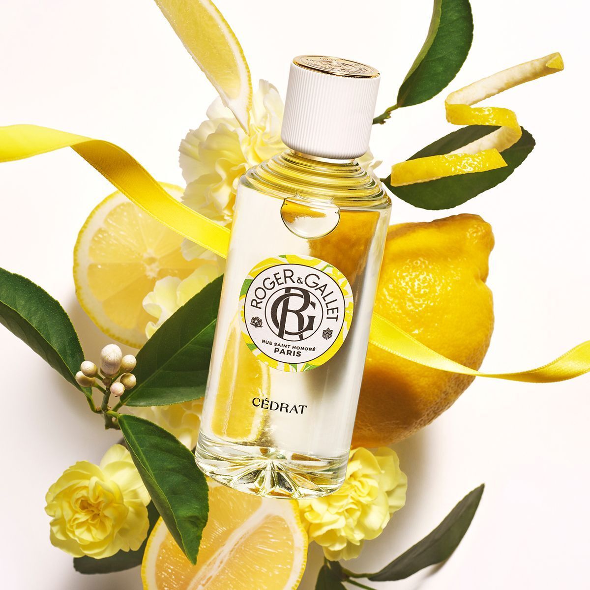 Roger & Gallet Cédrat parfumfles met witte dop, omringd door citroenen, bladeren en gele bloemen.