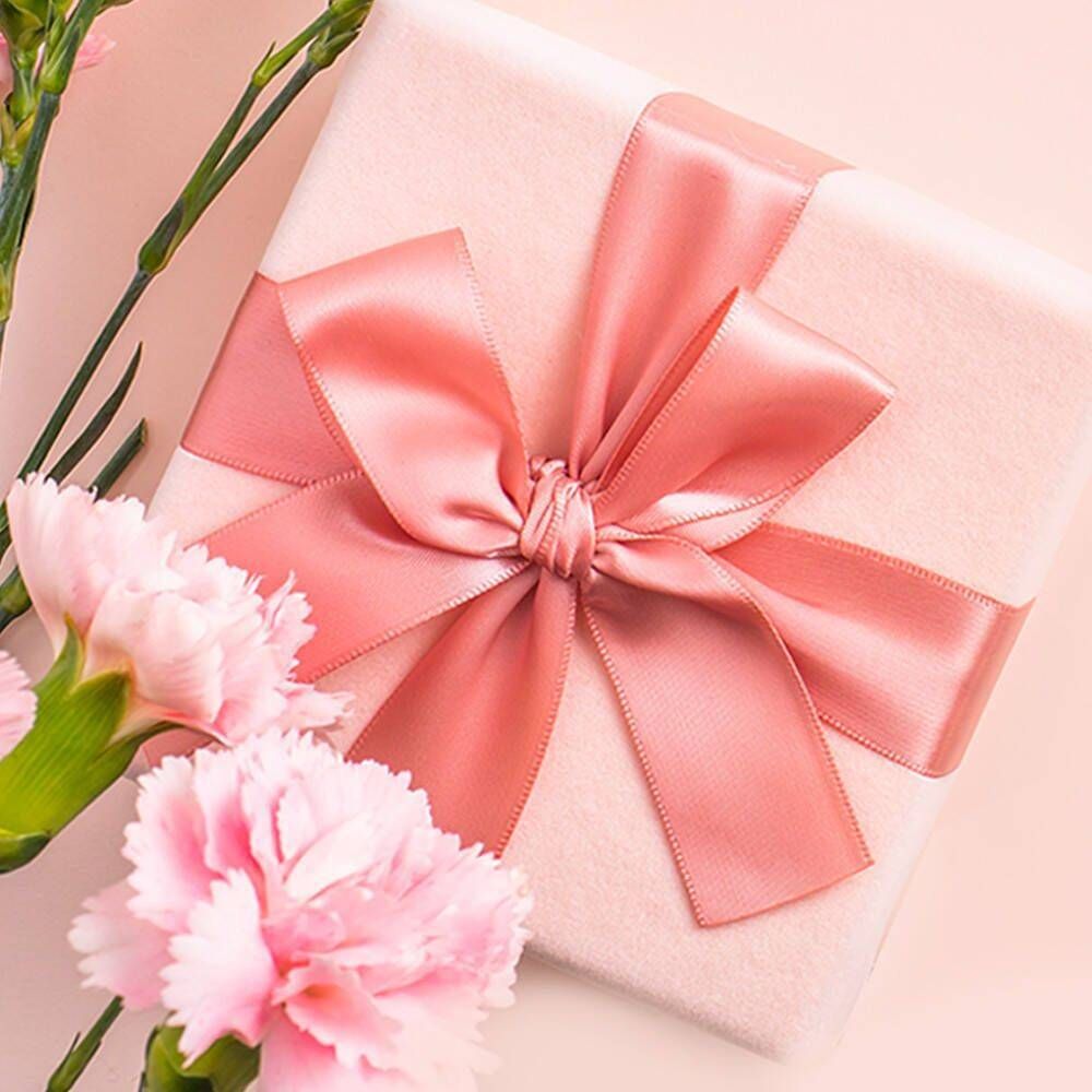 Boîte cadeau rose avec ruban. Des œillets roses sont à côté.