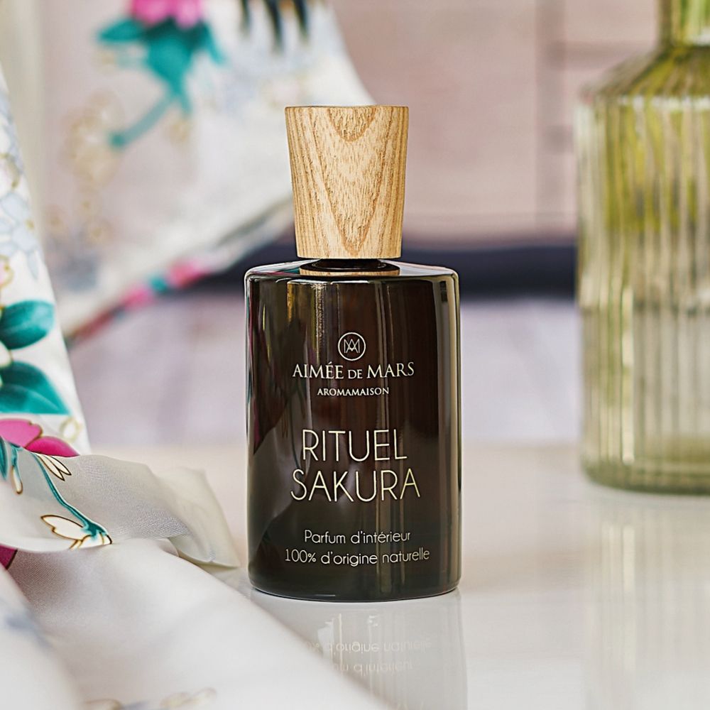 Bruine glazen fles met houten dop. Opschrift: RITUEL SAKURA, Parfum d'intérieur, 100% d'origine naturelle. Op tafel.