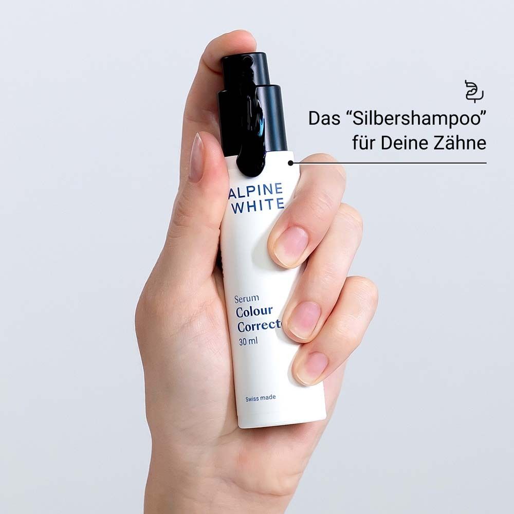 Hand houdt serumflesje vast. Tekst: ALPINE WHITE, Serum Colour Corrector, 30 ml. Zwarte dop.