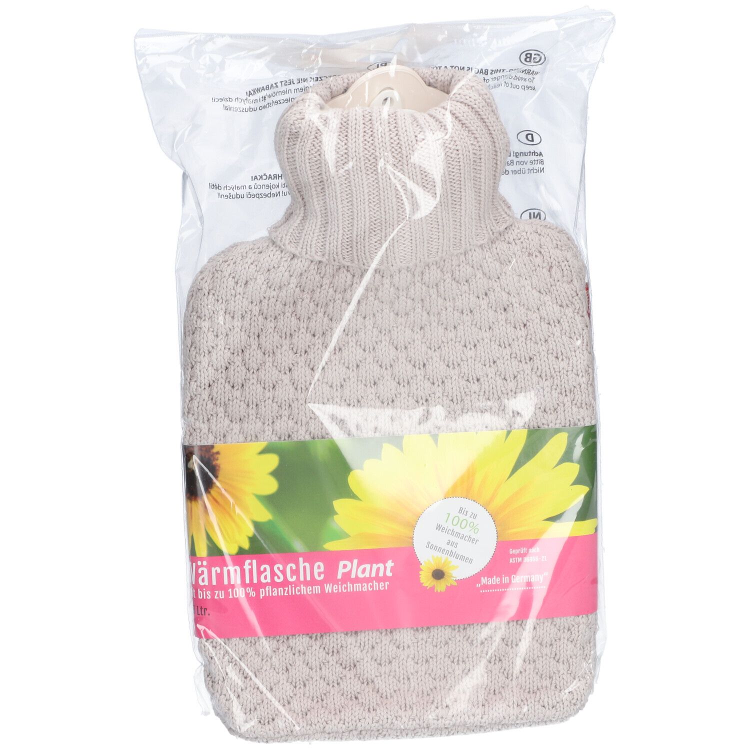 Warmwaterkruik in transparante verpakking. Beige gebreide hoes, groene band met logo en zonnebloem. Tekst: Warmwaterkruik Plant.