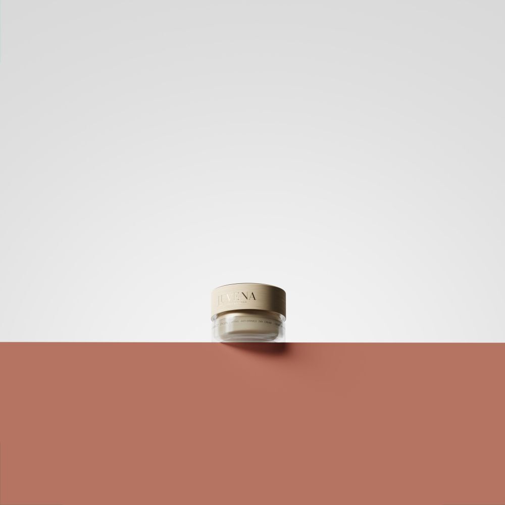 Petit pot de crème avec couvercle doré. Inscription : Juvena. Placé sur fond rouge et blanc.