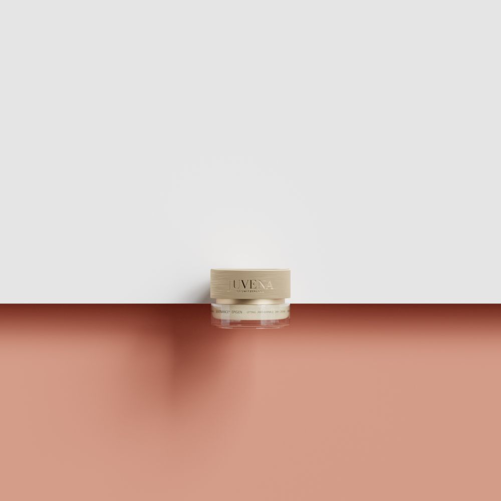 Petit pot de crème avec couvercle doré. Inscription : Juvena. Placé sur fond rouge et blanc.