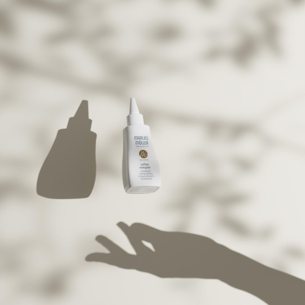 Witte fles met puntige applicator, zwevend. Schaduw van een hand en bladeren.