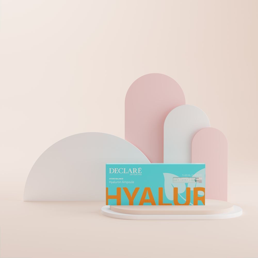 Boîte turquoise avec logo DECLARÉ et nom du produit. Placée sur un piédestal. Fond avec des formes roses et blanches.