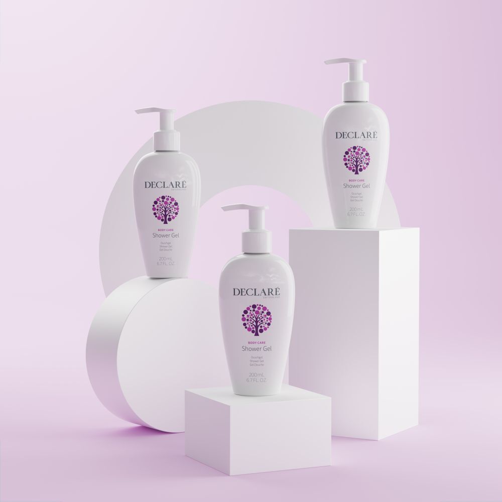 Drie witte DECLARÉ-flessen met pomp op sokkels. Achtergrond: witte vormen en roze vlak. Product: Shower Gel.