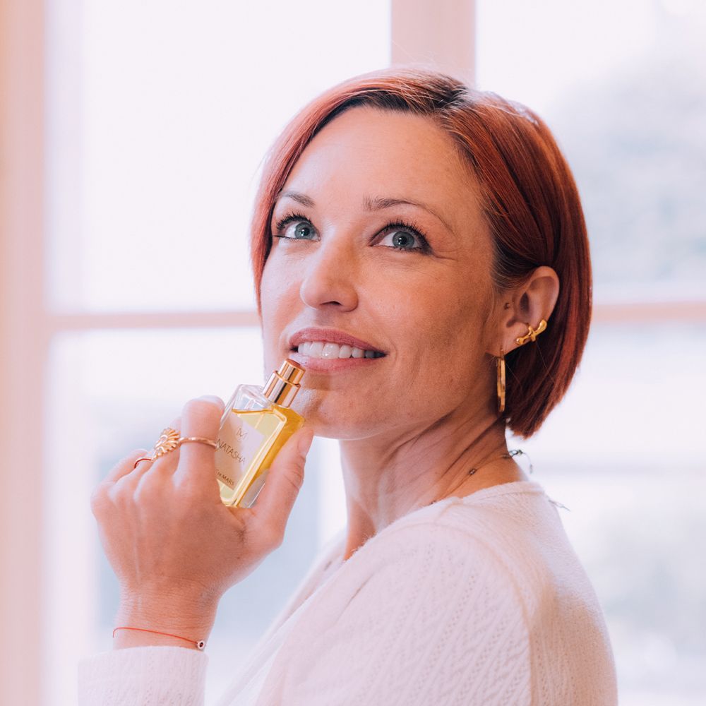 Femme tenant un flacon Aimée de Mars Natasha Eau de Parfum. Elle sourit, flacon près du visage.