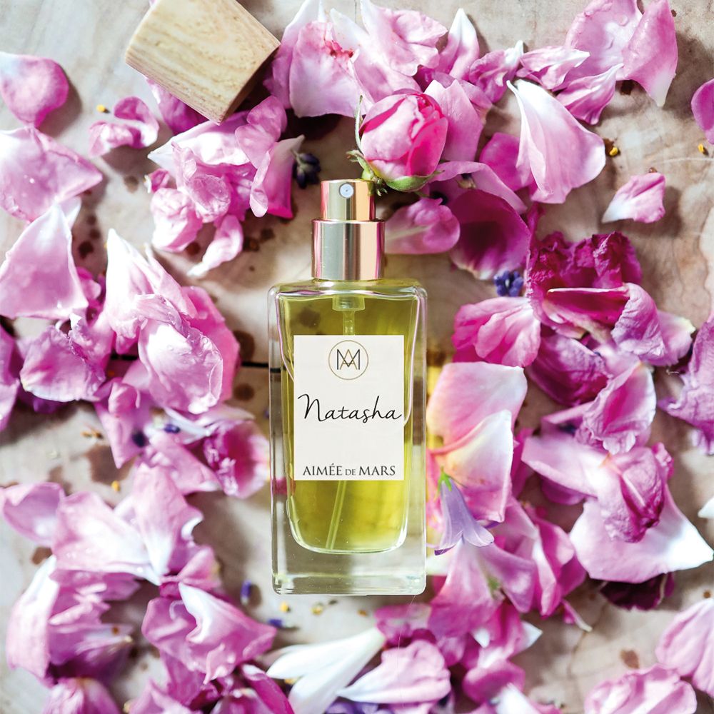 Flacon Aimée de Mars Natasha Eau de Parfum sur bois. Entouré de pétales roses. Vaporisateur doré.