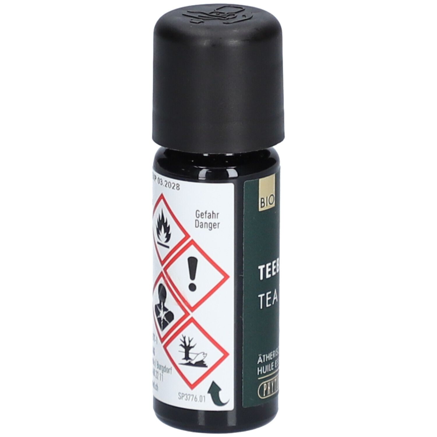 Bruine glazen fles met zwarte dop. Gevarensymbolen en opschrift: Tea Tree, etherische olie. Merk: PHYTOMED.