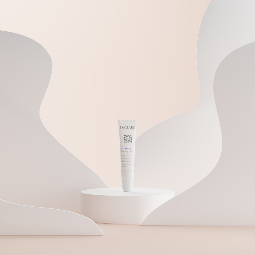 Tube blanc DECLARÉ Eye Contour Firming Cream sur socle blanc. Fond avec formes blanches.