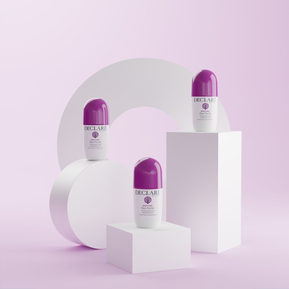 Trois roll-ons Deo Forte sur socles blancs. Fond : formes blanches et roses. Bouchons violets visibles.