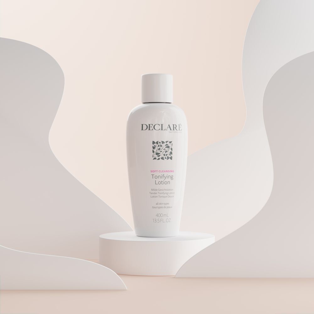 Witte fles met dop op een sokkel. Opschrift: DECLARÉ, logo, Toning Lotion. Achtergrond met witte en beige vormen.